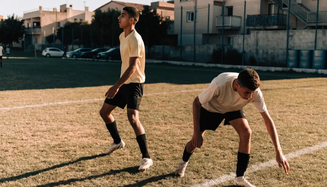 שני מגני כדורגל ישראלים צעירים עומדים בקו הגנה במגרש קהילתי, עוקבים אחרי הכדור וקוראים את המשחק יחד