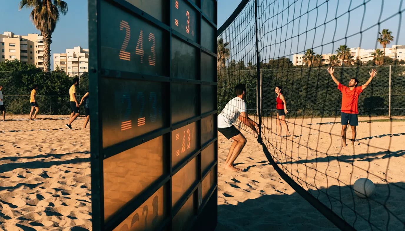 שחקני כדורעף ישראלים במגרש קהילתי בוחנים את לוח התוצאות ליד הרשת באור יום ים תיכוני